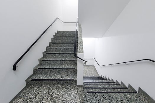 Minimalist interior view of a granite staircase with black handrails, featuring clean white walls.